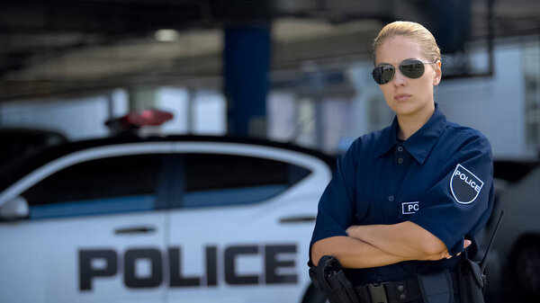Serious policewoman putting on sunglasses and posing on camera, public safety