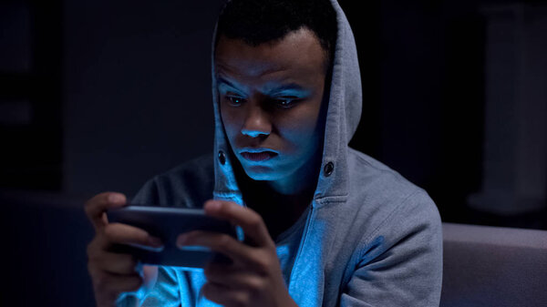 Black teenager playing video games on phone, harm for mental health and eyesight