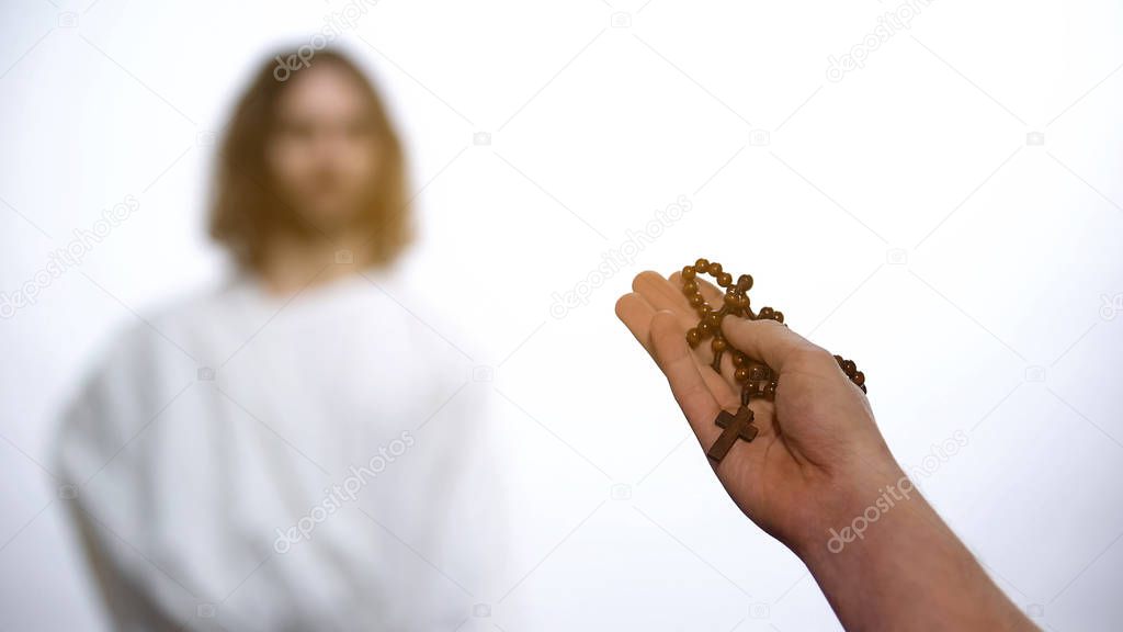 Male hands holding Rosary, praying to appeared God on background, salvation