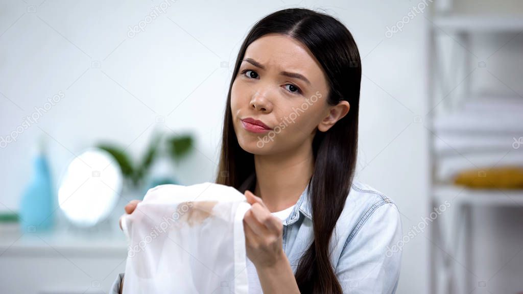 Upset asian housewife showing coffee stain on shirt at camera, laundry service