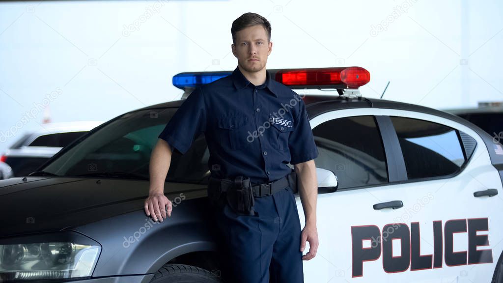 Serious policeman in uniform leaning on patrol car, maintenance of order, duty