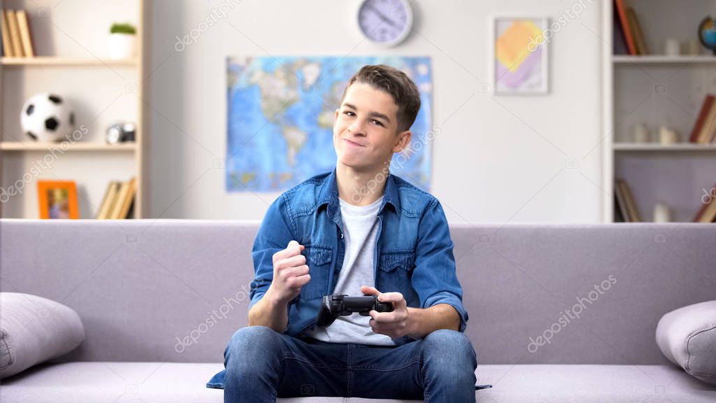 Teen boy with joystick clenching fist, disappointed about losing video game