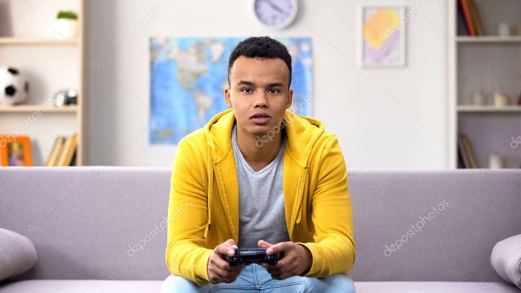 Addicted African-American teenager playing computer game, lack of emotions