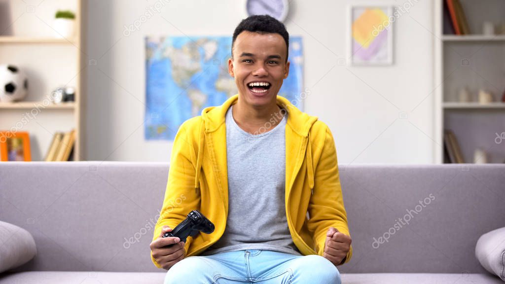 Mixed-race teen boy playing video game rejoicing victory, leisure time at home