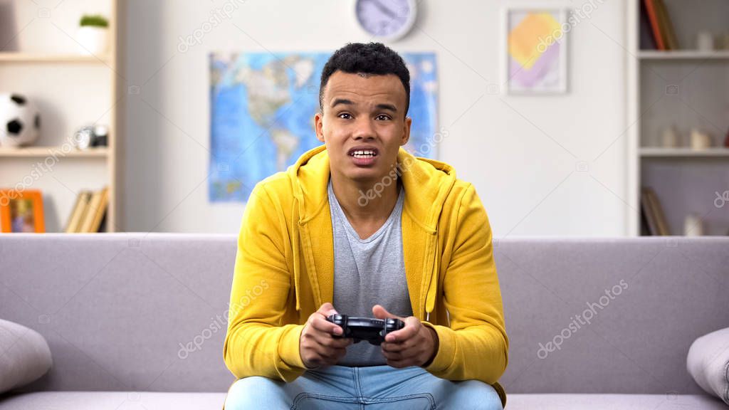 Dissatisfied mixed-race teenager boy playing video game, losing level, addiction