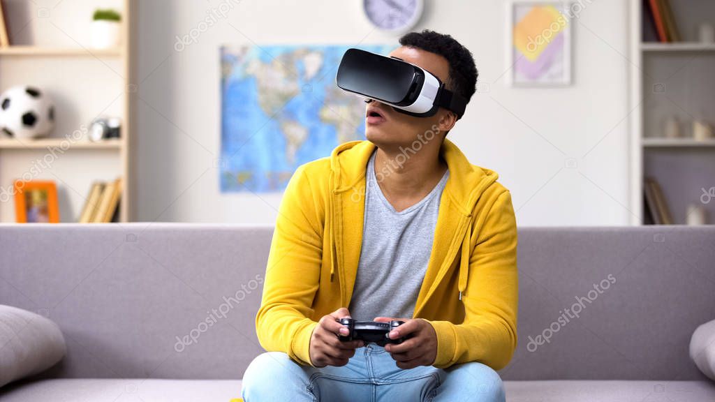 African-American teen boy with joystick playing video game in VR headset, future