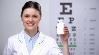 Dostu kadın optometrist görme desteği için vitamin ile şişe gösteren