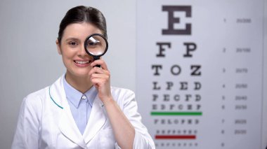 Gülümseyen optometrist büyüteç ve gülümseyerek bakarak, görme testi