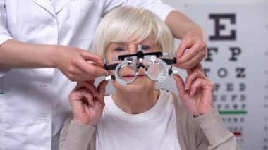 Optisyen tutan phoropter, yaşlı kadın görme muayenesi için hazırlanıyor, sağlık