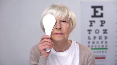Senior woman clothing eye and squeezing at camera, risk of cataract in old age clipart