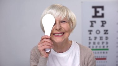Retired female closing eye and smiling to camera, successful cataract surgery clipart