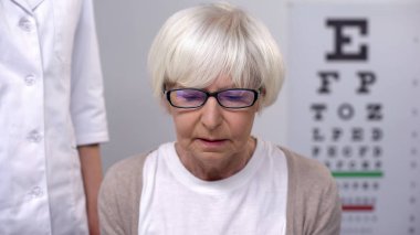 Depressed old woman in eyeglasses on ophthalmologist appointment, vision problem clipart