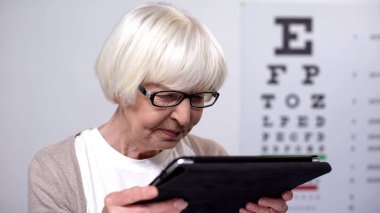 Buruşuk yaşlı kadın sekmesini tutarak ve okumaya çalışıyor, kötü görme ile mutsuz
