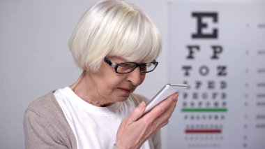 Yaşlı kadın akıllı telefon, küçük yazı tipi, kötü görme sorunu okumaya çalışıyor