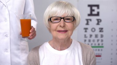 Optisyen mutlu yaşlı bayan taze havuç suyu veren, iyi görme bakımı
