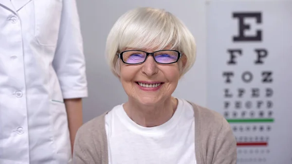 微笑的老年妇女在眼镜看着相机 适当的镜头选择 — 图库照片