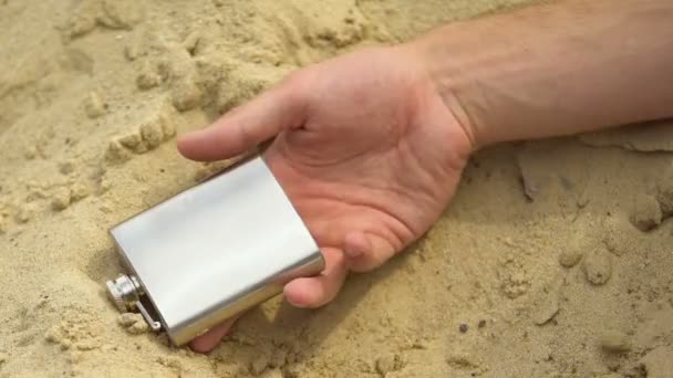 Hand holding heupfles vallen op zand, dodelijke alcoholintoxicatie in de woestijn — Stockvideo
