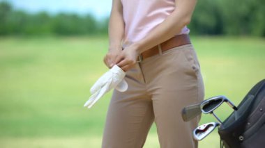 Yetenekli kadın golf oyuncusu yakındaki demir kulüpleri ile beyaz eldiven çanta giyiyor, hobi