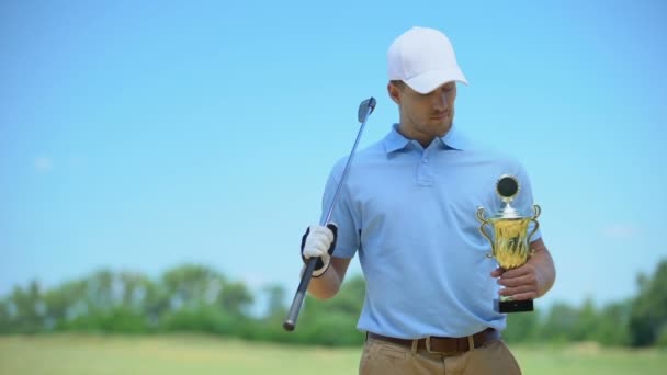 Selbstbewusster Golfspieler mit Goldpokal und Schläger, der in die Kamera lächelt, Sportmeister — Stockvideo