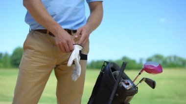 Maçtan önce beyaz eldiven giyen erkek golfçü, yakındaki spor malzemeleri ile çanta