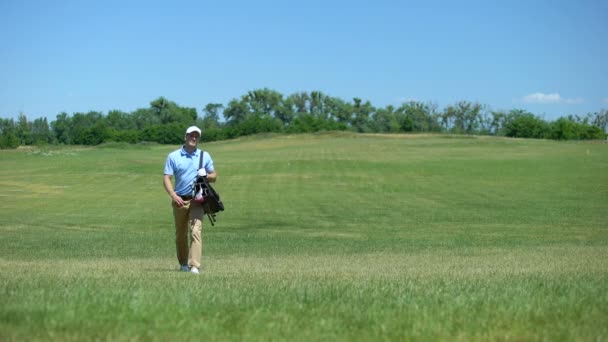 Профессиональный тренер по гольфу ходит по полю с клубной сумкой для отдыха — стоковое видео