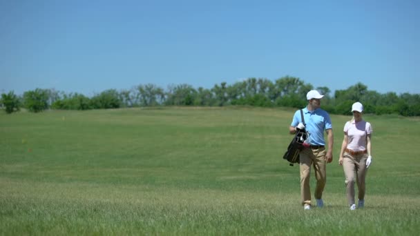 Par de golfistas com saco de clubes se comunicando durante a caminhada do curso após o hobby do jogo — Vídeo de Stock