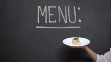 El Menü arka plan üzerinde pasta ile plaka tutar, restoranda lezzetli tatlılar