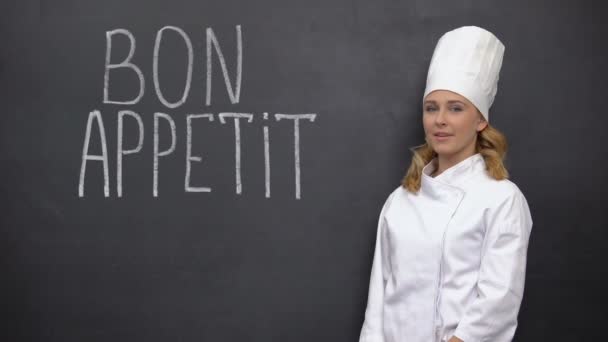Vrouwelijke chef-kok staat in de buurt van Bon appetit Franse zin, adverteren van Elite keuken — Stockvideo