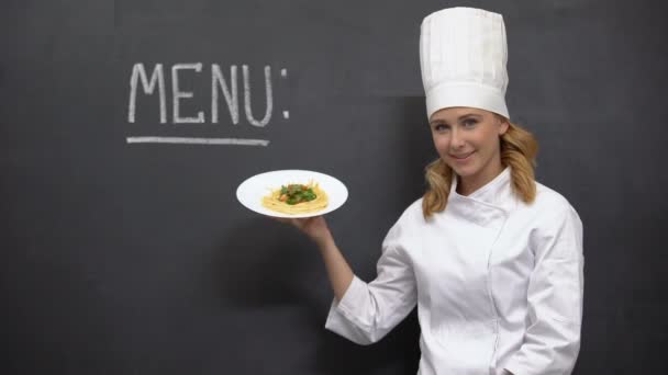 Женщина шеф-повар держа тарелку макарон с меню слово на доске, ресторан — стоковое видео