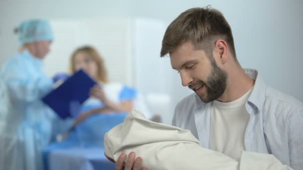 Buon padre che tiene in braccio il bambino appena nato durante l'infermiera spiegando la moglie dopo il parto — Video Stock