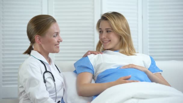 Усміхнений акушер і вагітна жінка тримає животик, дивлячись на камеру — стокове відео