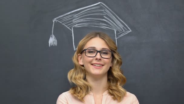Mujer de pie cerca de pizarra con sombrero de graduación dibujado sobre la cabeza, la educación — Vídeo de stock