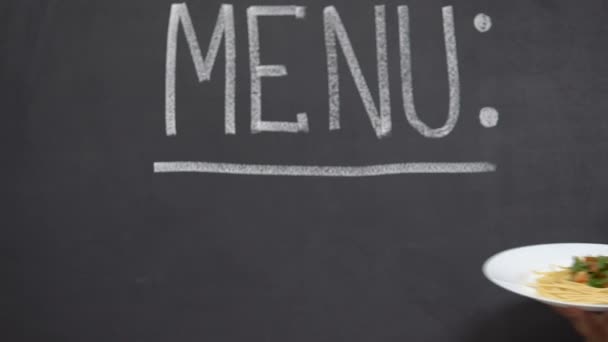 Hand showing plate with delicious pasta, menu written on blackboard, restaurant — Stock Video