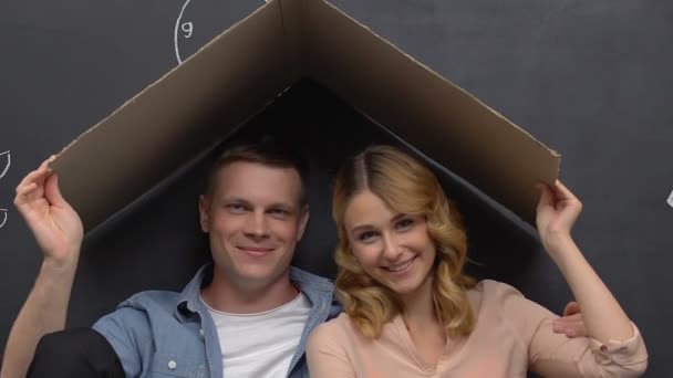 Чоловік і дружина, сидячи під дахом картону, мріють про дім — стокове відео