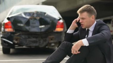 Üzgün erkek sürücü sinirli araba kazasındasonra sigorta şirketi ile telefon konuşuyor