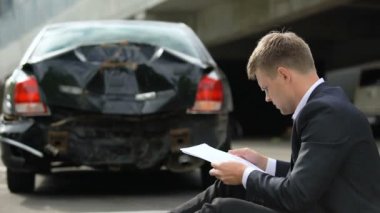 Erkek sürücü yolda oturan, araba kazasında sonra sigorta sözleşmesi ile bakıyor