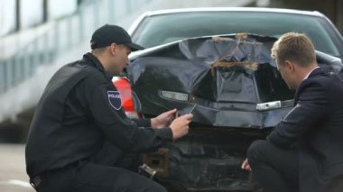 Kaza yıkan araba fotoğraflarını gösteren polis memuru, araba kazasında suçlu bulunan erkek sürücüye