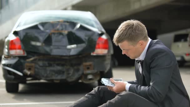 Hombre contando dólares, mirando daños coche tras accidente, reparaciones costo — Vídeo de stock