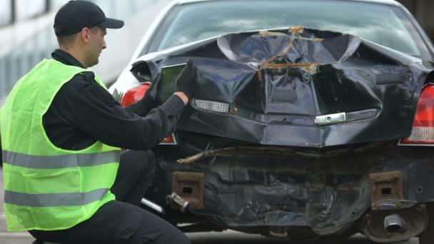 Сотрудник страховой компании фотографирует повреждение автомобиля с помощью планшетного компьютера, несчастный случай — стоковое видео