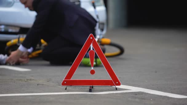 Panneau rouge d'urgence sur la route, conducteur mâle vérifiant le pouls de la victime de l'accident de voiture, mort — Video