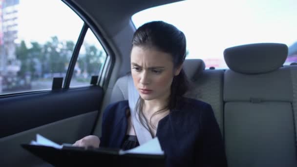 Tired woman in suit looking through documents and feeling migraine riding in car — Stock Video
