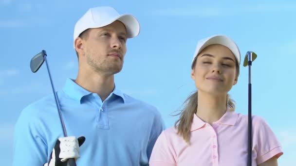 Inspirerade manliga och kvinnliga golfspelare med klubbar som tittar på distans på banan — Stockvideo
