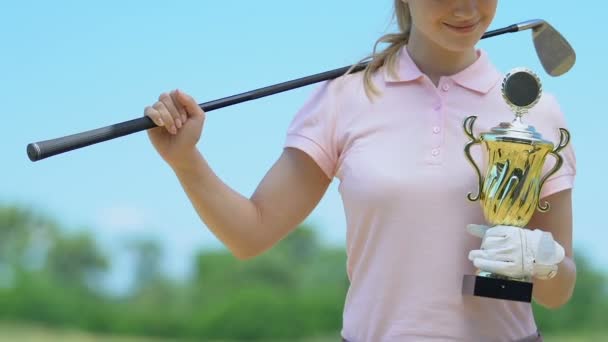 Улыбающаяся девочка-гольфист позирует держа золотую чашу, довольная победой, триумфом — стоковое видео