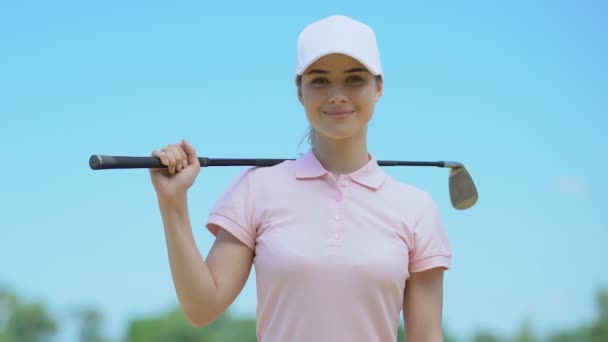 Счастливая девушка с клюшкой для гольфа в руке, улыбаясь позируя перед камерой, довольная игрой — стоковое видео