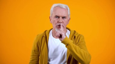 Gri saçlı emekli turuncu arka plan, gizli karşı sessizlik jest gösteren