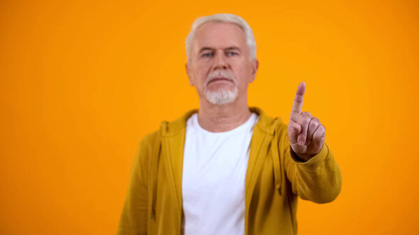Elderly male in casual clothes showing warning finger gesture, rejection sign
