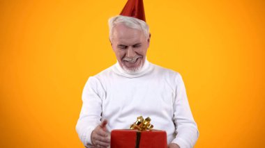 Şaşırmış yaşlı erkek kırmızı hediye kutusuna bakıyor, şu an için mutlu, doğum günü