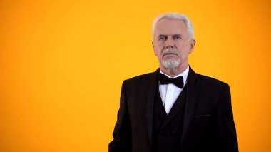 Sarı arka planda duran takım elbiseli ciddi yaşlı adam, randevuya hazırlanıyor