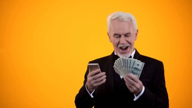 Takım elbiseli mutlu emekli adam cep telefonu online bahis yapma, nakit ödül sevinir