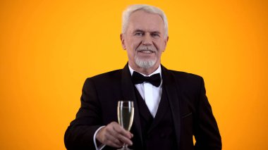 İçecek bardağı tutan ve gülümseyen, flört eden takım elbiseli akıllı kıdemli beyefendi